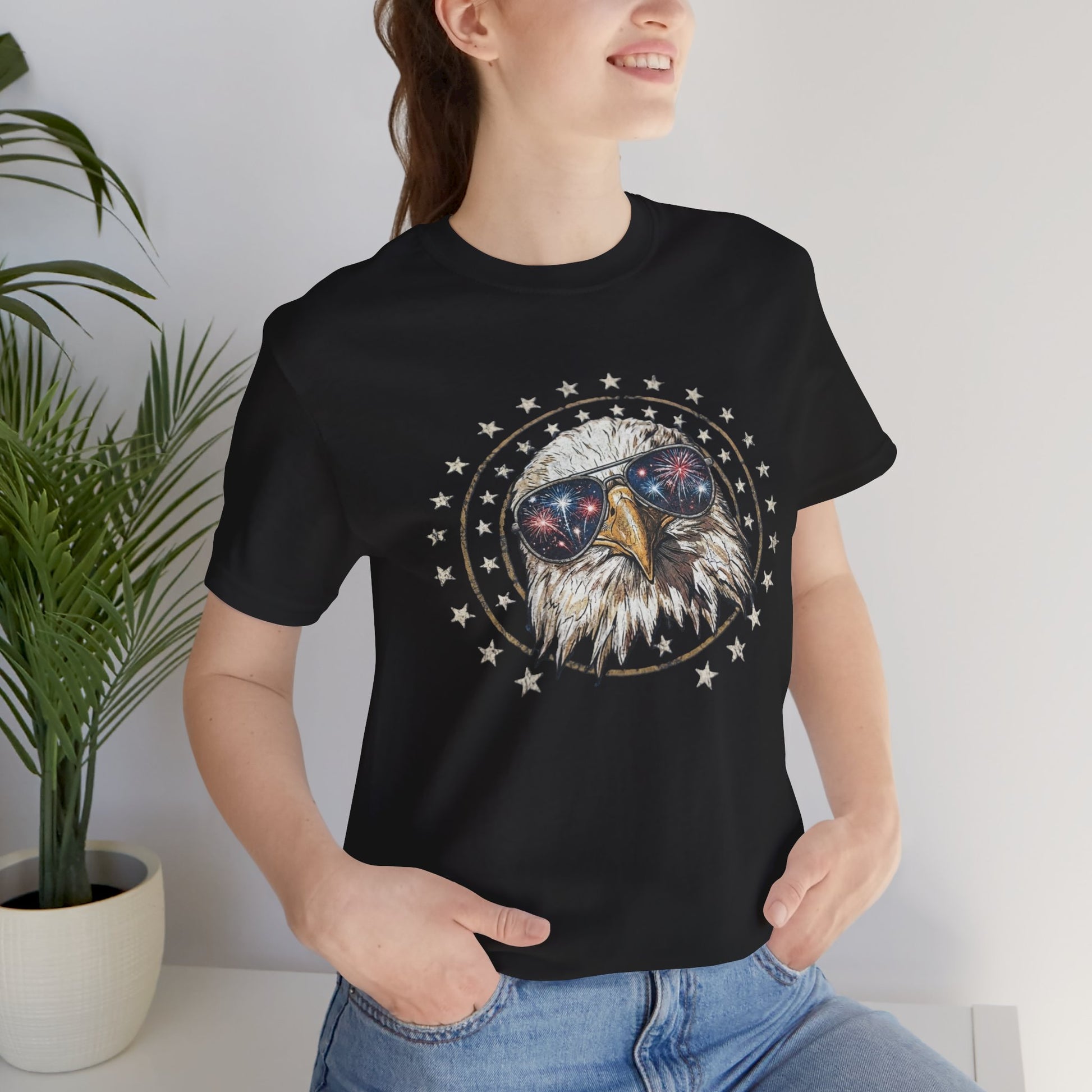 Close-up graphic design of a majestic bald eagle wearing black aviator sunglasses that reflect red, white, and blue fireworks, encircled by a distressed ring of  stars against a solid black background.