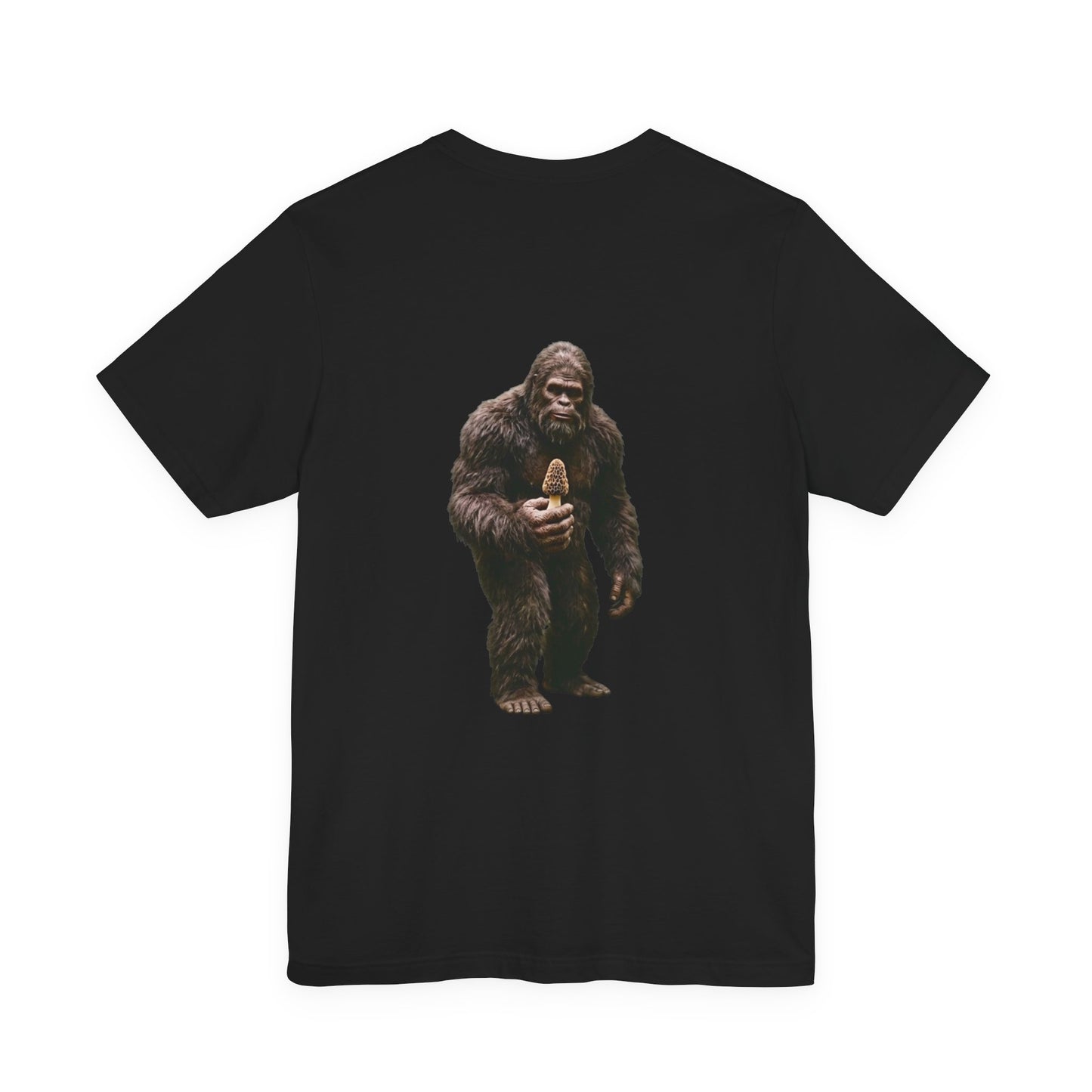 Hyper-realistic full body graphic of Bigfoot standing against a solid black background and holding a single yellow morel mushroom on a t-shirt.